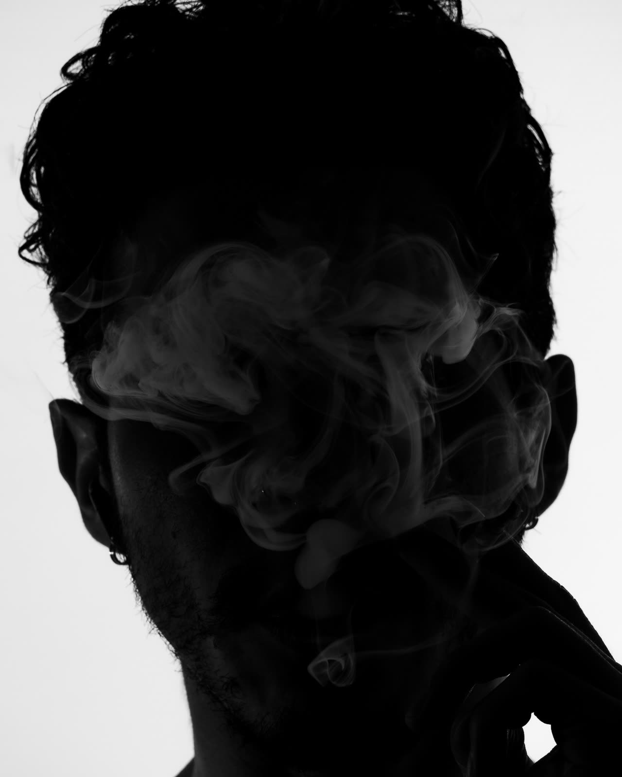 Retrato en blanco y negro de un rostro en contraluz envuelto en humo