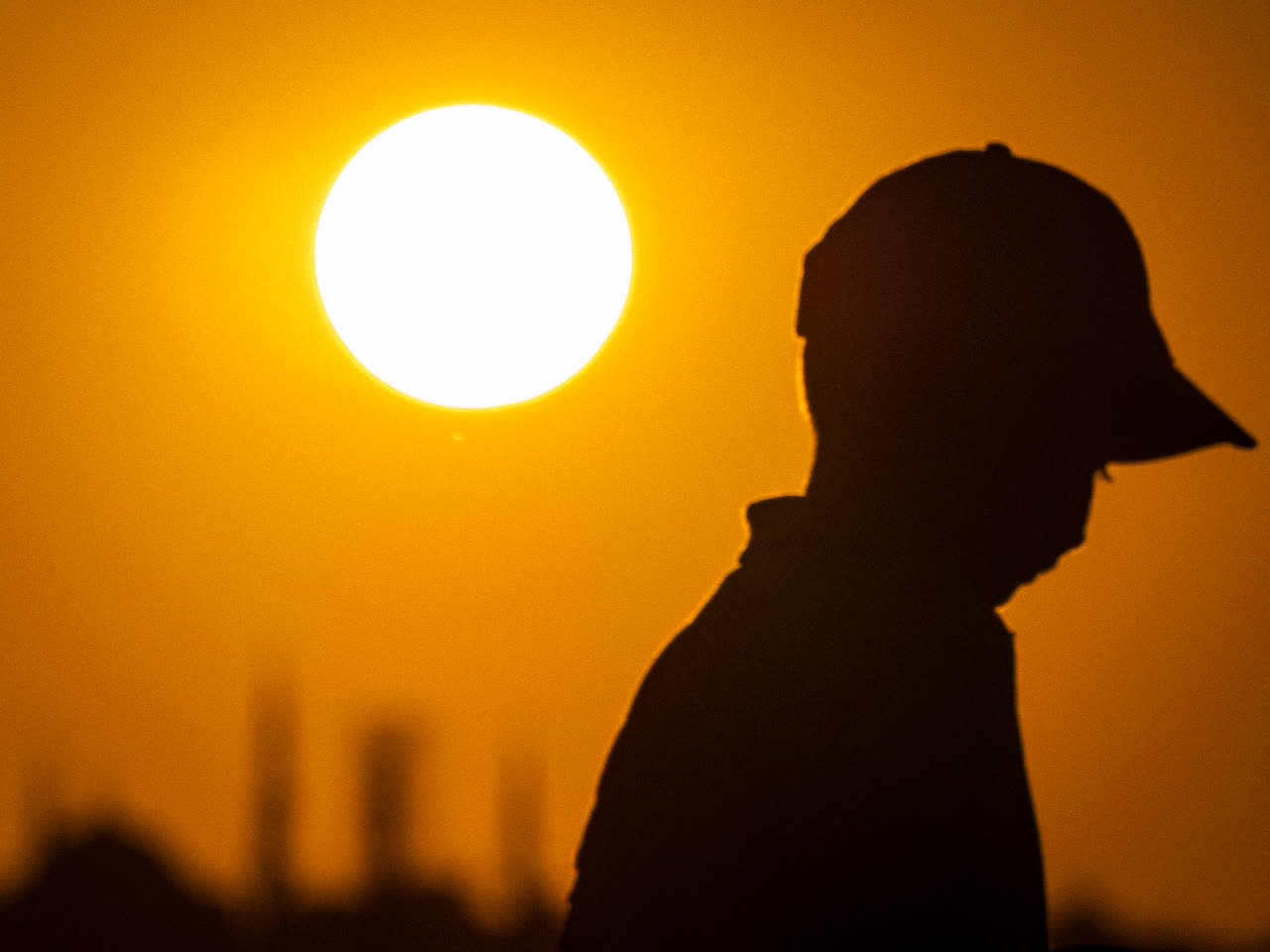 Silueta de una persona con gorra frente al sol al atardecer