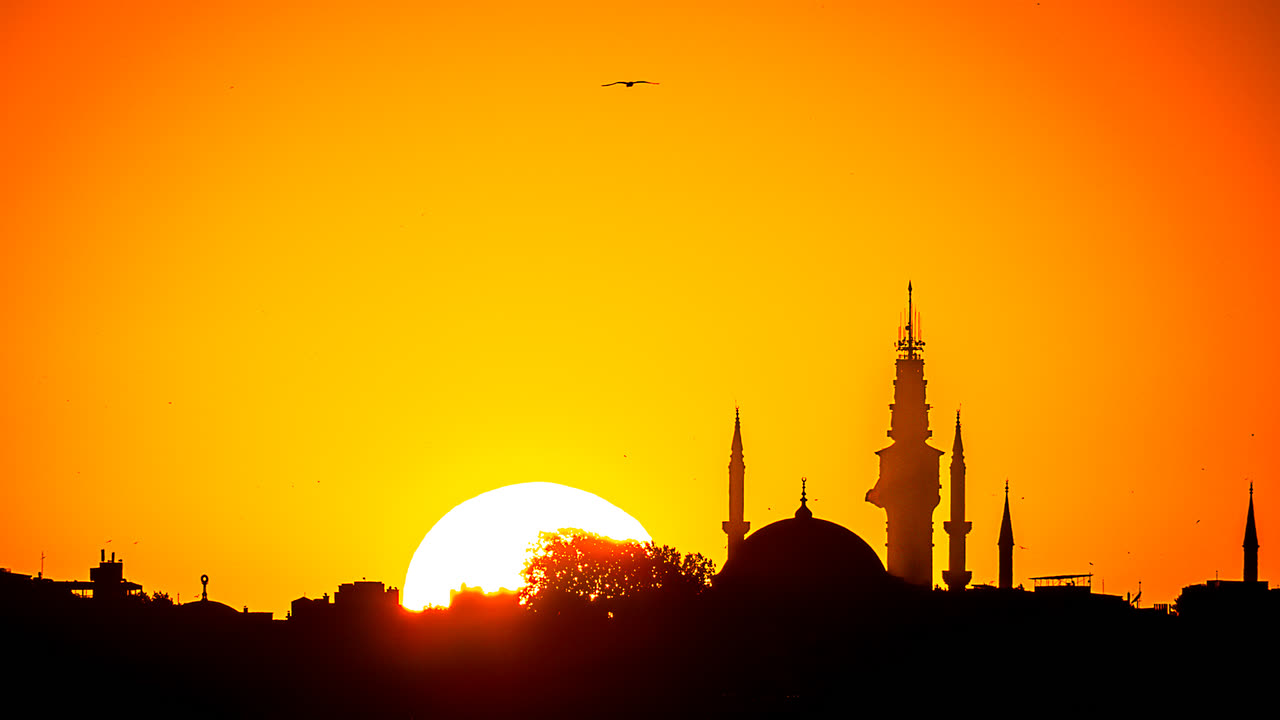 Silueta de una ciudad con minaretes recortada sobre un cielo naranja