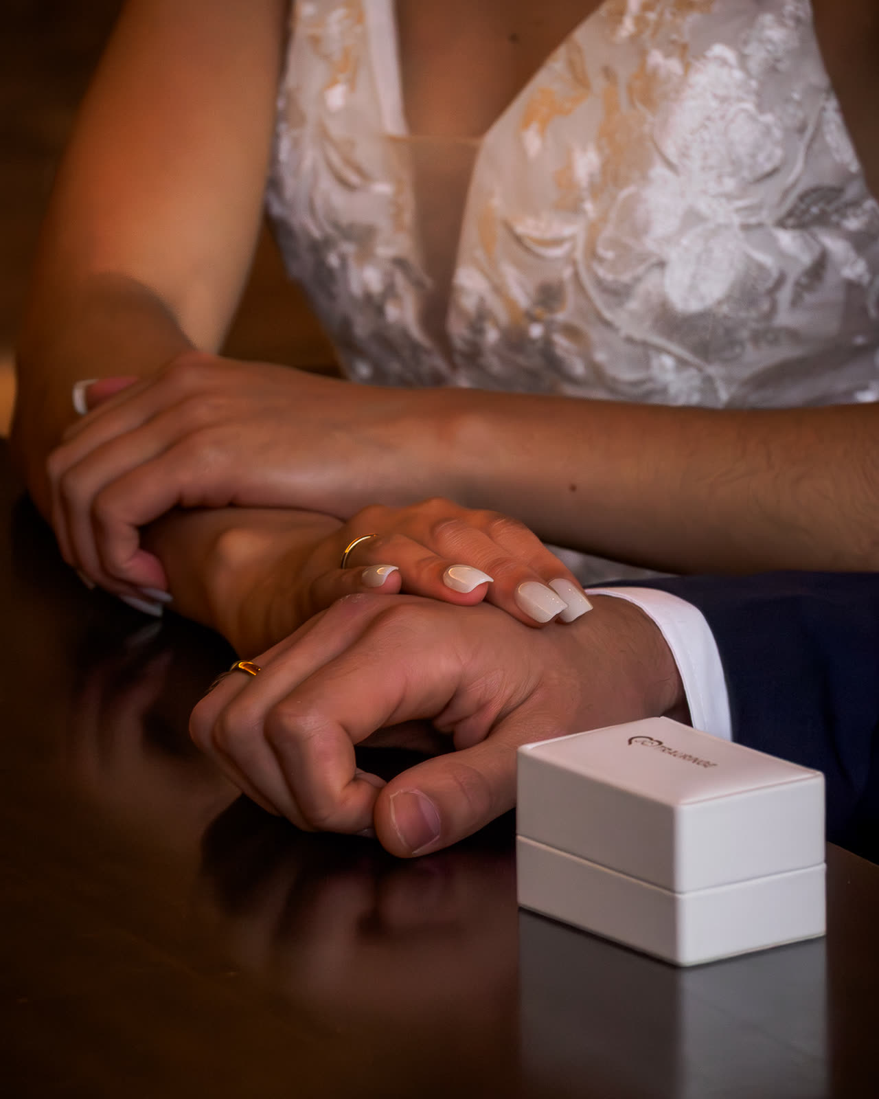 Manos entrelazadas de una pareja de novios junto a la caja de los anillos
