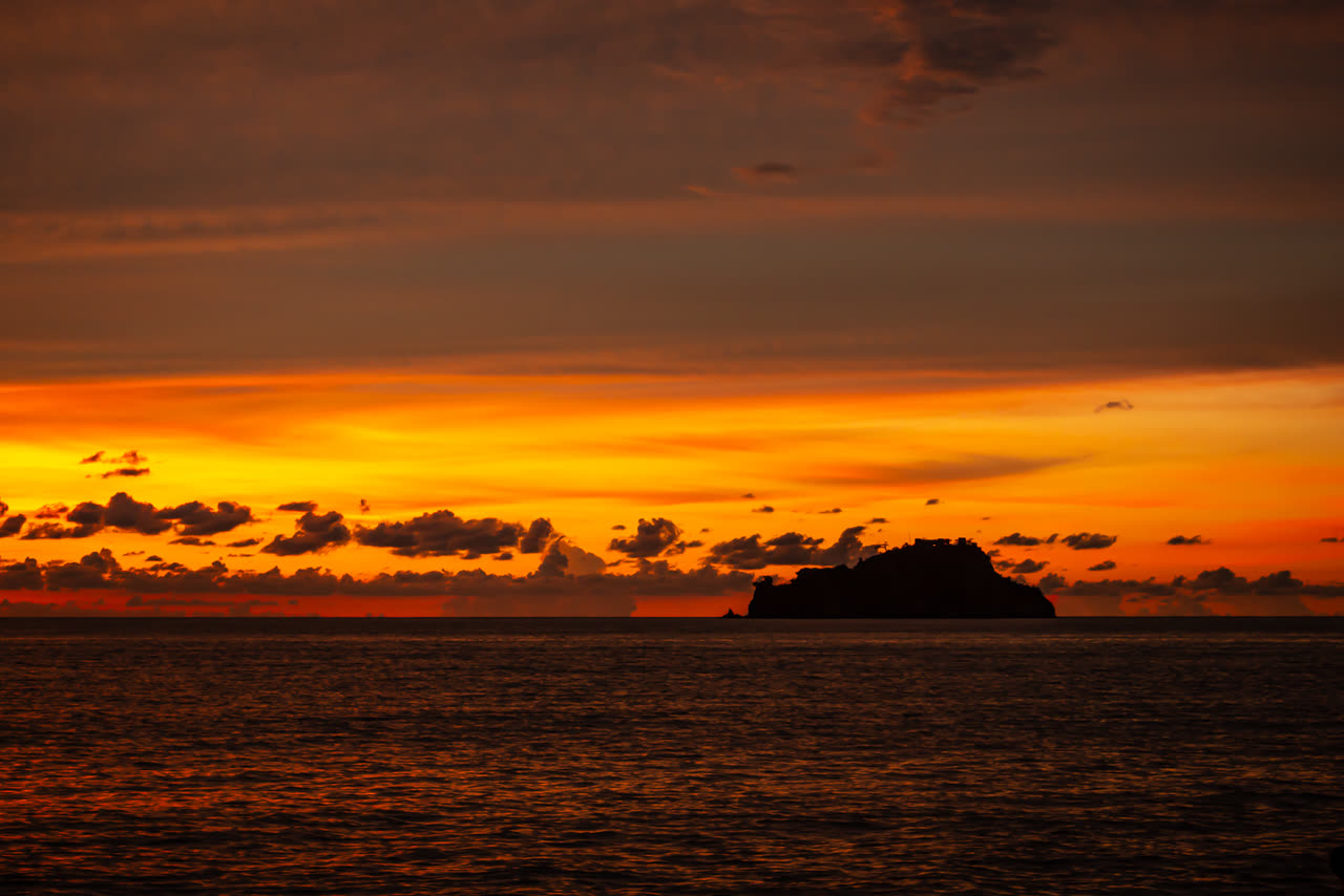 Isla recortada sobre un atardecer naranja en el mar