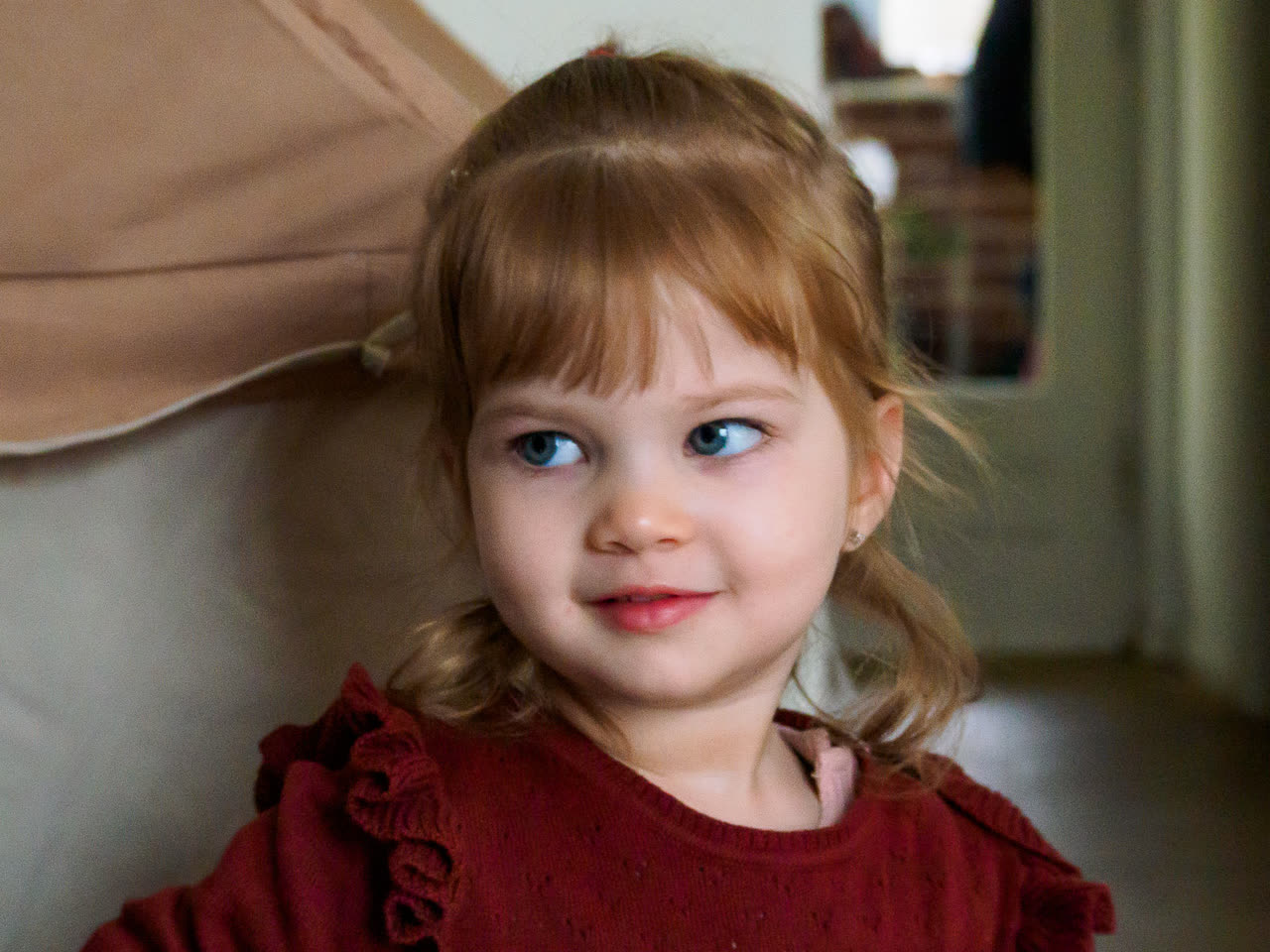 Niña pequeña de jersey rojo mirando hacia un lado con la mirada perdida