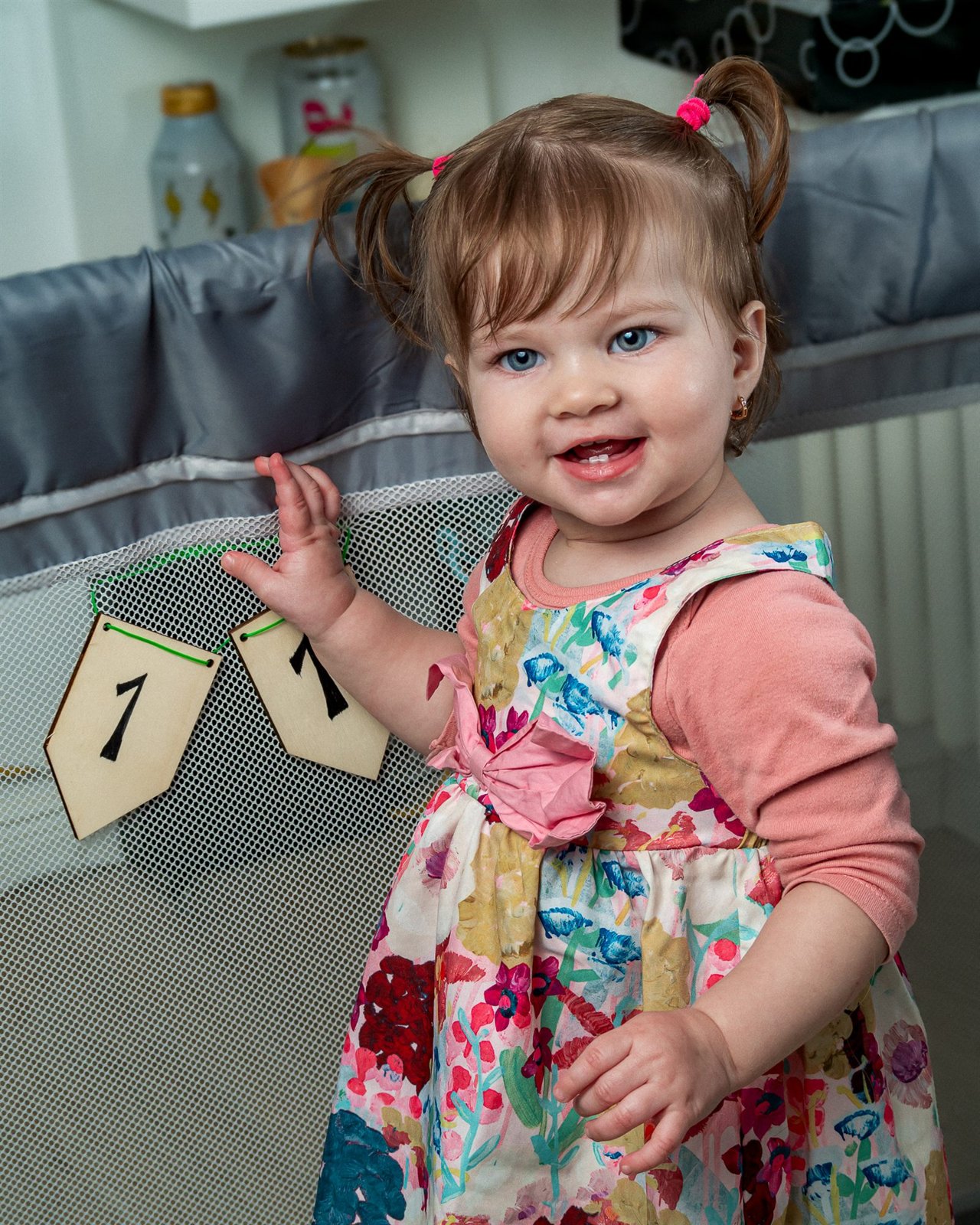 Niña pequeña con coletas y vestido de flores sonriendo junto a un banderín de su primer cumpleaños