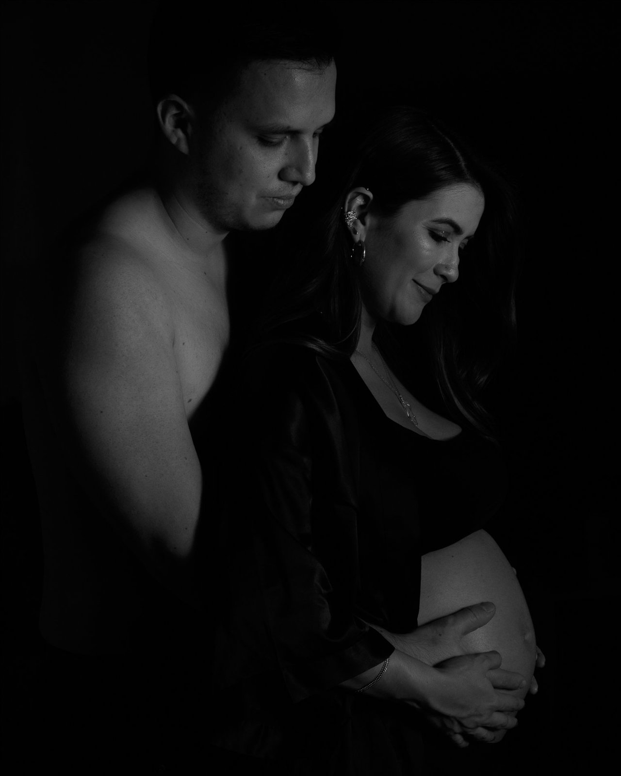 Retrato en blanco y negro de una pareja abrazada sobre el vientre embarazado