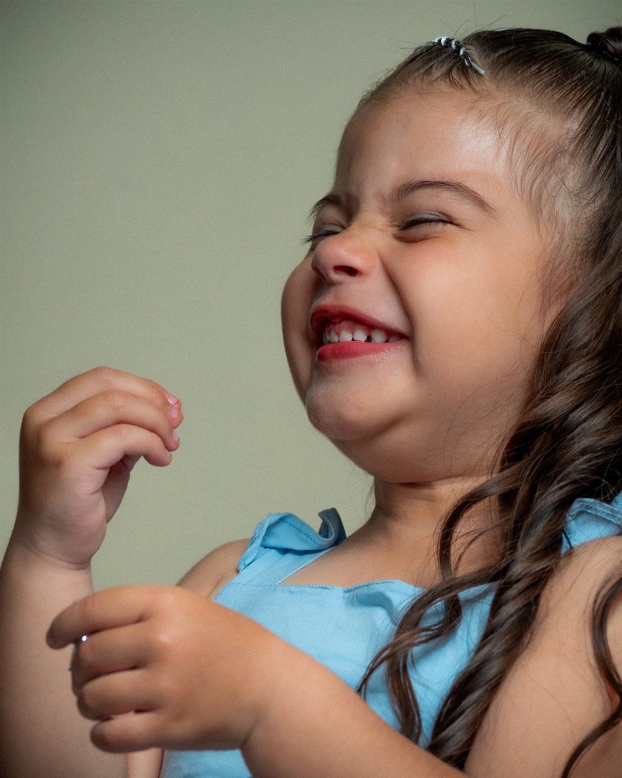 Niña con vestido celeste riendo a carcajadas con los ojos cerrados