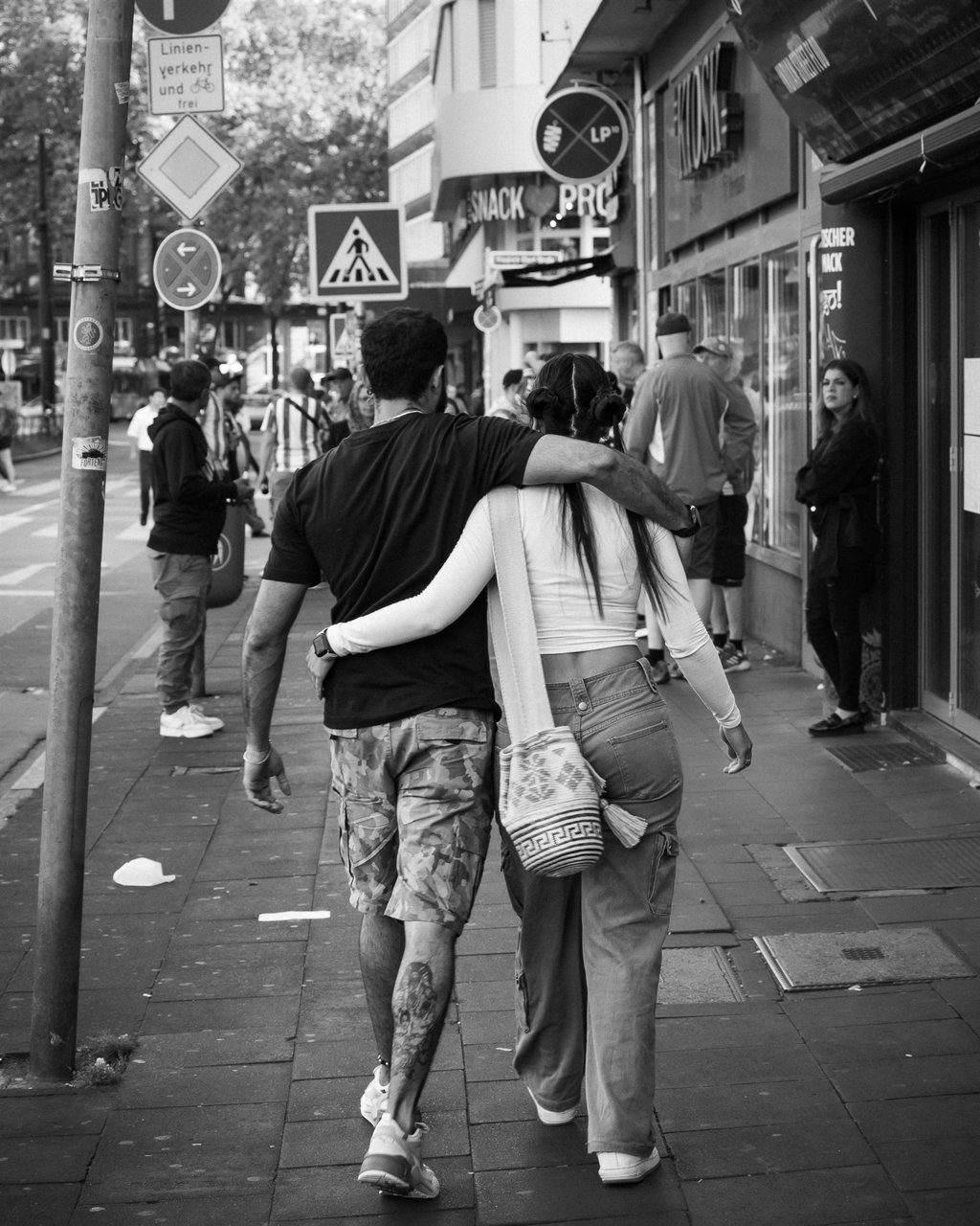 Pareja abrazada caminando de espaldas por una calle concurrida, en blanco y negro