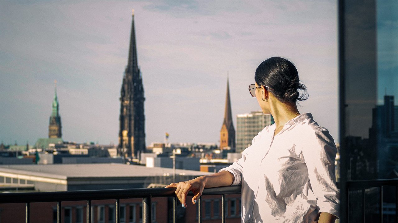 Mujer de blusa blanca contemplando las agujas de la ciudad desde una terraza