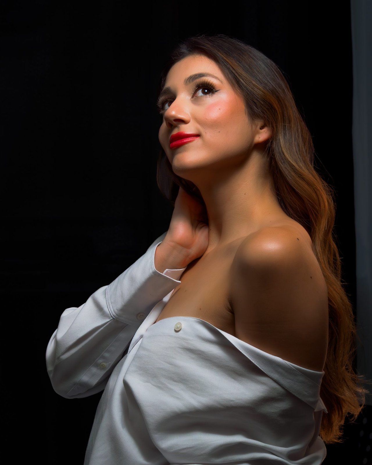 Mujer de labios rojos y camisa blanca sobre el hombro mirando hacia arriba sobre fondo negro