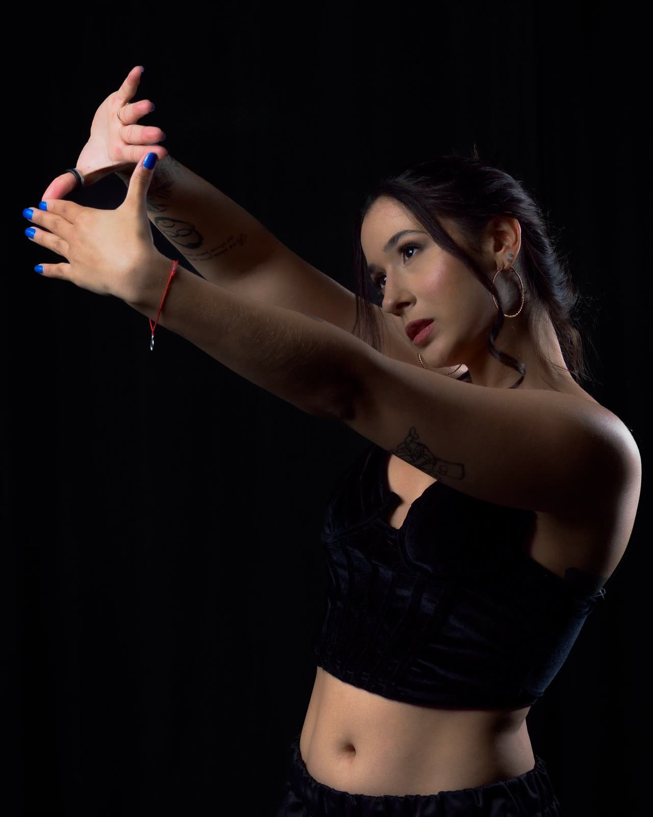 Mujer con top negro extendiendo los brazos con las manos entrelazadas sobre fondo negro