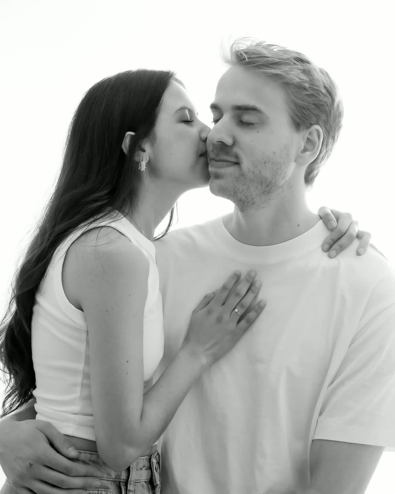 Pareja abrazada en blanco y negro; ella le besa la mejilla